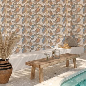 May include: A patterned wall featuring abstract shapes in beige, orange, blue, and brown. The image shows a wooden bench, a vase with dried plants, and a pool with clear water. A straw hat and cushion are on the bench, creating a relaxing outdoor scene.