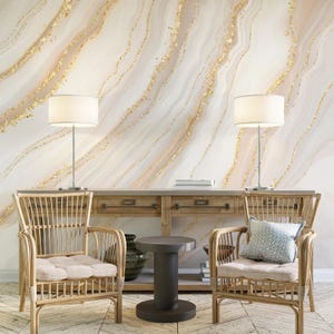 Könnte beinhalten: Zimmerinterieur mit Marmoreffekt-Tapete und goldenen Akzenten. Zwei Rattan-Sessel mit beigen Kissen flankieren einen dunkelgrauen Beistelltisch. Eine Holzkonsolentisch mit Büchern und einer Vase, mit zwei Lampen.