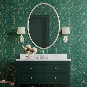 Pode incluir: Uma bancada de banheiro com um armário verde escuro, bancada de mármore branco e espelho oval. As paredes são cobertas com papel de parede verde com redemoinhos dourados. Duas arandelas com abajures creme ladeiam o espelho. Um vaso de flores está sobre a bancada.