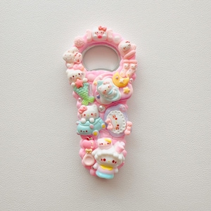 Pu&ograve; includere: Un apribottiglie rosa decorato con varie figure in miniatura di Hello Kitty, tra cui una sirena, un personaggio che dorme su una luna e altri piccoli ciondoli. La superficie &egrave; strutturata con molteplici decorazioni in plastica dai toni plastica color pastello.