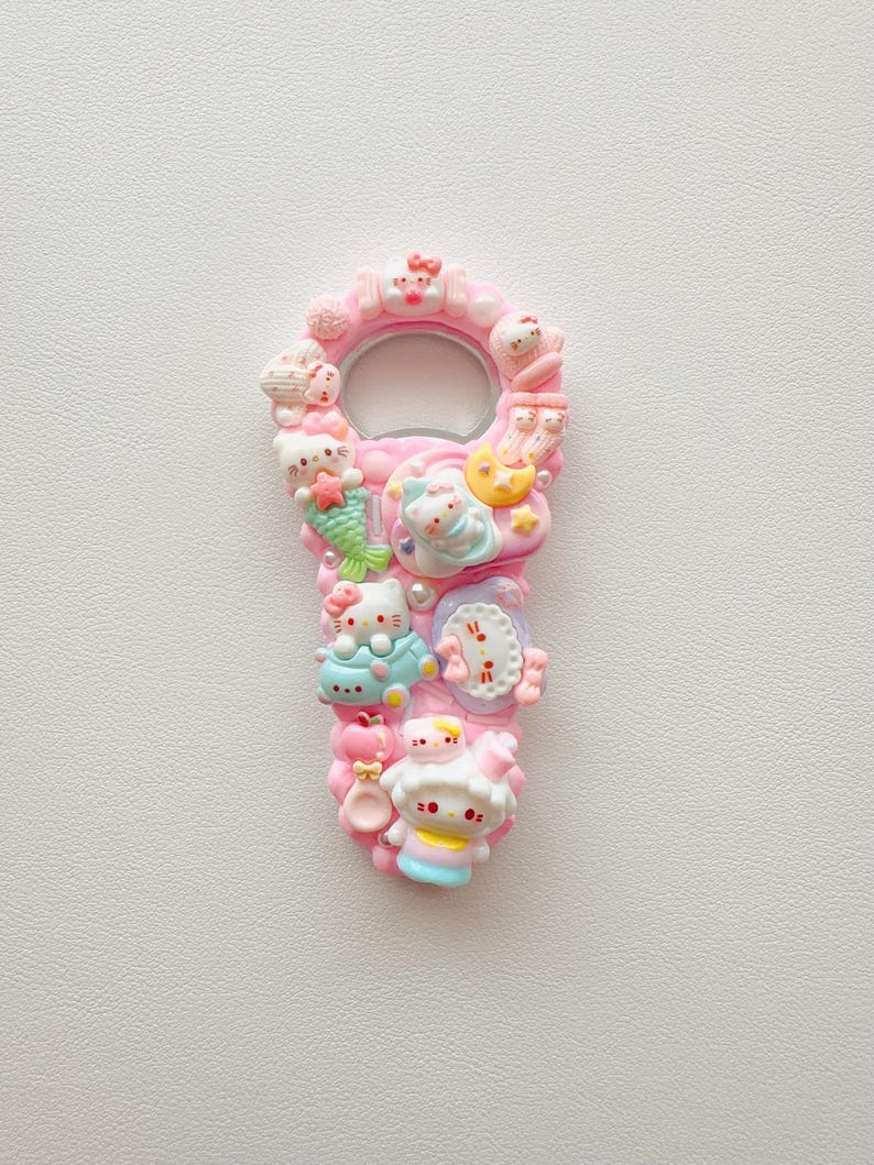 Pu&ograve; includere: Un apribottiglie rosa decorato con varie figure in miniatura di Hello Kitty, tra cui una sirena, un personaggio che dorme su una luna e altri piccoli ciondoli. La superficie &egrave; strutturata con molteplici decorazioni in plastica dai toni plastica color pastello.