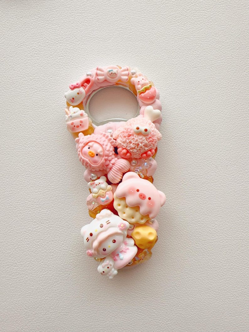 Pu&ograve; includere: Un apribottiglie decorato con varie figurine in miniatura di colore rosa e pastello, tra cui un personaggio gatto, un maiale, un pesce e una creatura soffice. La superficie &egrave; impreziosita da piccole perline e ciondoli nei toni del rosa, bianco e giallo.
