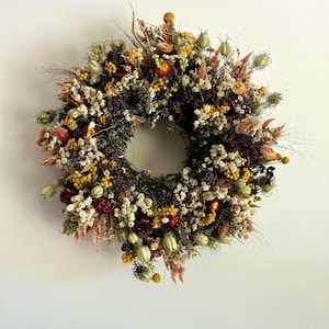 May include: A circular wreath made from dried flowers and foliage. The wreath displays a variety of textures and colours, including yellow, white, red, and brown. The wreath is likely used for home decor, adding a natural touch to any space.