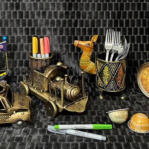 May include: A collection of decorative metal desk organizers and holders. Includes a truck, train, boat, bicycle, and clock, all in antique gold tones. Also features a camel figurine, pen holders, and a utensil holder.