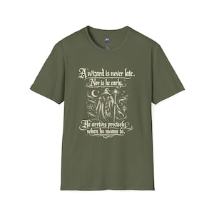 Op de afbeelding: Olijfgroen t-shirt met een afbeelding van een tovenaar met staf, maan en sterren. De tekst luidt: "Een tovenaar komt nooit te laat. Ook niet te vroeg. Hij komt precies wanneer hij het wil."