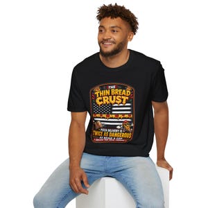 May include: Black t-shirt featuring a graphic of an American flag made of pizza slices and the text "The Thin Bread Crust." Below the flag graphic is the text "Pizza delivery is twice as dangerous as being a cop."