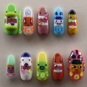 May include: A collection of ten colorful, cartoon-like nail art designs. Each nail features a unique character with expressive faces, bright colors, and decorative elements. The designs include various shapes and sizes, showcasing creative nail art.