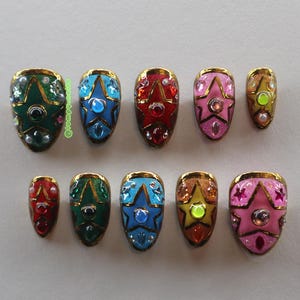 May include: Ten star-shaped nail art designs, each with a gold border and embellished with gems and glitter. The nails feature a variety of colours including green, blue, red, pink, and gold. The design creates a glamorous and eye-catching look.