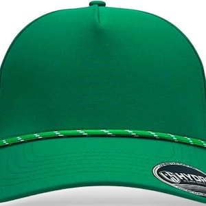 Pode incluir: Boné verde liso com aba reta e detalhe de corda branca e verde na frente. O boné tem uma aba curva e um pequeno botão redondo na parte superior. Um logotipo é visível na aba.