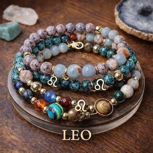 May include: A stack of three beaded bracelets featuring various natural stone beads in shades of blue, brown, grey, and orange, accented with gold-toned metal spacers and charms depicting the Leo zodiac symbol. The word LEO is printed below.
