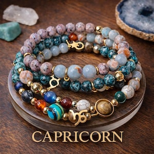 May include: A multi-strand beaded bracelet featuring various natural stone beads in shades of blue, brown, white, and orange, accented with gold-toned metal spacers and charms, including a Capricorn zodiac symbol and the text CAPRICORN.