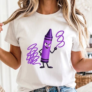 May include: A white short-sleeved t-shirt featuring a graphic of a purple crayon character with a mischievous facial expression, arms, and legs. The character is depicted drawing purple scribbles and loops on the fabric of the shirt.