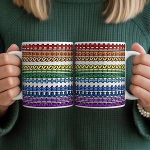 May include: Two white ceramic mugs with colorful, patterned designs. Each mug features a repeating pattern of horizontal bands in various colors, including red, orange, yellow, green, blue, and purple. The mugs have white handles.