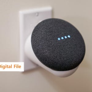 Puede incluir: Un altavoz inteligente gris oscuro con una cubierta de tela, montado en un adaptador de toma de corriente de pared blanco. El altavoz muestra cuatro luces azules. El texto "Digital File" está en un cuadro blanco.