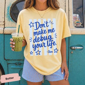 May include: A pale yellow short-sleeve t-shirt featuring blue vertical stripes and the blue text "Don't make me debug your life. -Stem" surrounded by small blue stars. The shirt is paired with blue and white vertical striped shorts.