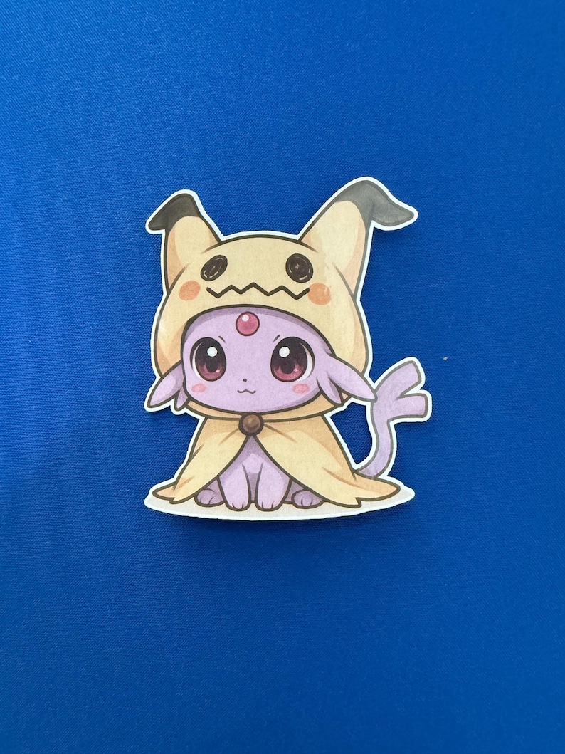 May include: A sticker featuring a cartoon character in a Mimikyu costume. The character is purple with large, pink eyes and a yellow hooded cloak. The background is a solid blue.