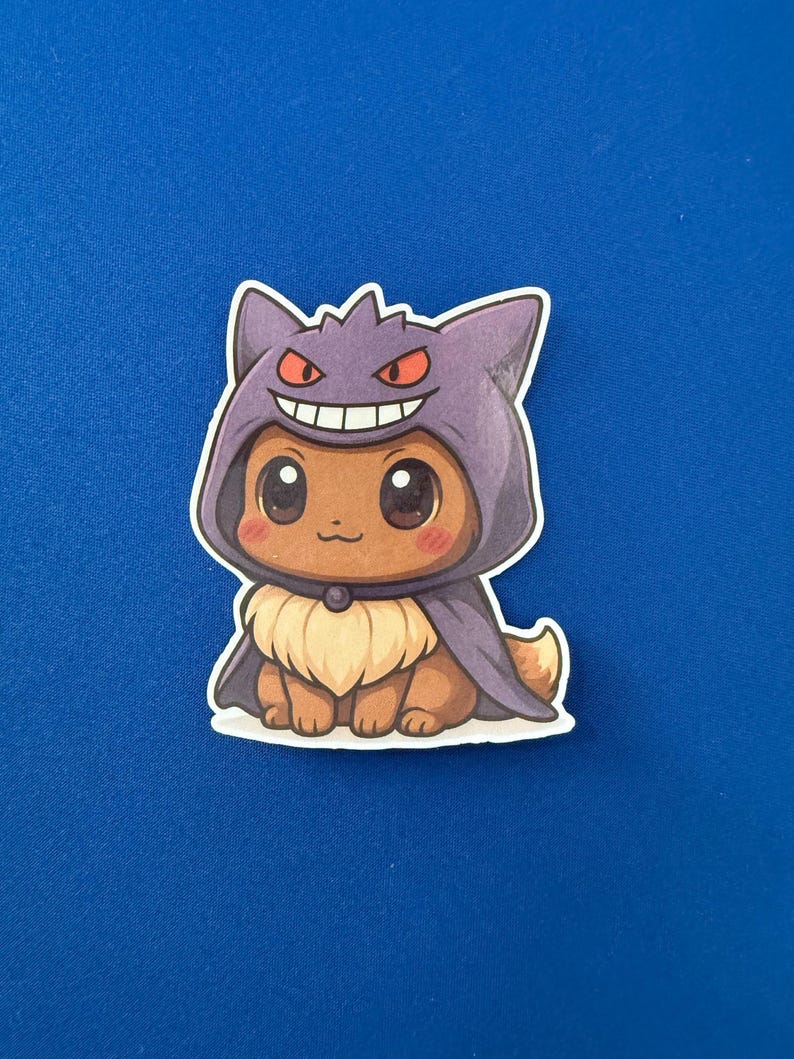 May include: A sticker featuring a cartoon character in a purple hooded cloak with red eyes and a smiling mouth. The character has brown fur, large eyes, and a cream-colored chest. The sticker is on a blue background.