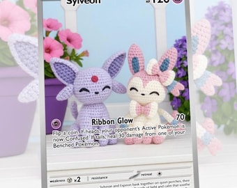 May include: A Pokémon trading card featuring two crocheted Sylveon figures. The card displays the name "Sylveon" at the top, with "HP 120" and "Ribbon Glow" text. The figures are lavender and pink, with a white background and floral accents.