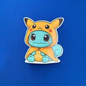 May include: A sticker featuring a cartoon Squirtle character dressed in a Pikachu costume. The Squirtle is light blue with a yellow and orange Pikachu hood and cape. The sticker is on a blue background.