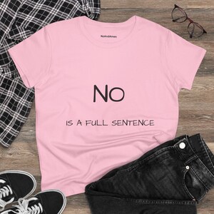 May include: A light pink t-shirt with the text "No is a full sentence" in black. The shirt is displayed with black jeans, black and white sneakers, and glasses.