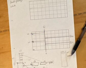 May include: A sheet of paper with architectural sketches and measurements. The text "Paint glossy white" is written at the top. A pen rests on the paper, which is on a wooden surface.