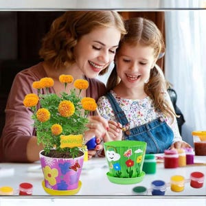 May include: A vibrant image of a marigold plant in a decorative pot with a yellow saucer. The pot is decorated with colorful flowers and butterflies. A second green pot with a painted landscape is also visible. Paint pots and brushes are on the table.