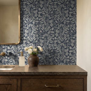 May include: Wallpaper featuring a repeating pattern of light gray leaves, stems, and small flowers against a dark navy blue background. The design covers the wall behind a bathroom vanity, which includes a dark wood cabinet and a dark countertop.
