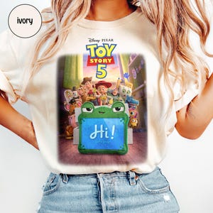 Puede incluir: Camiseta de color marfil con el dise&ntilde;o del cartel de la pel&iacute;cula Disney Pixar Toy Story 5. El dise&ntilde;o incluye el t&iacute;tulo de la pel&iacute;cula, personajes y un letrero con forma de rana que dice "Hi! Let's play!"