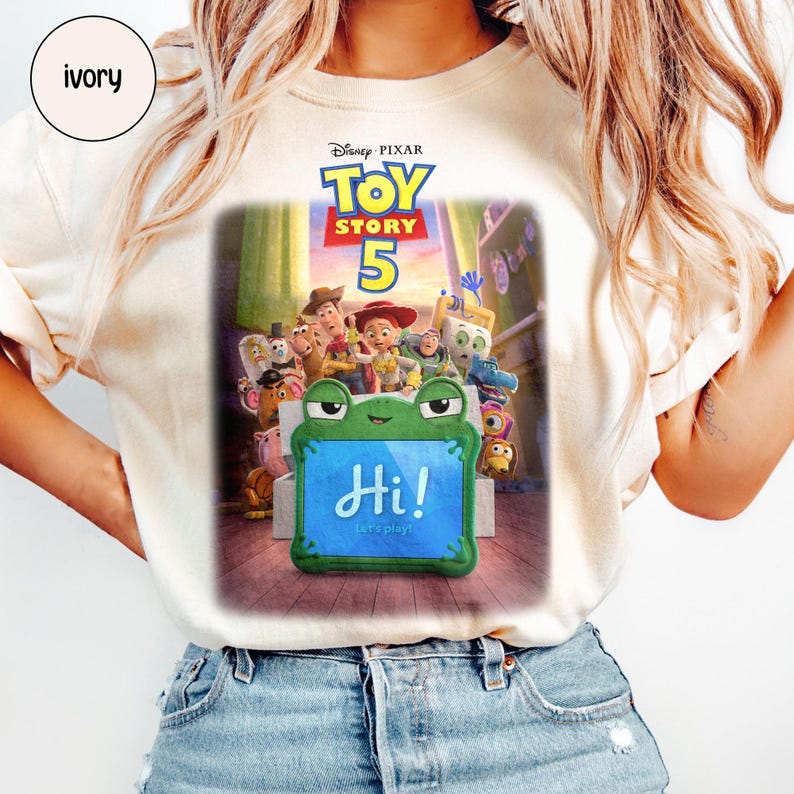 Puede incluir: Camiseta de color marfil con el dise&ntilde;o del cartel de la pel&iacute;cula Disney Pixar Toy Story 5. El dise&ntilde;o incluye el t&iacute;tulo de la pel&iacute;cula, personajes y un letrero con forma de rana que dice "Hi! Let's play!"