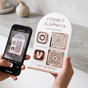 May include: An arched white acrylic sign with rose gold accents featuring the text CONNECT & FIND US, SCAN FOR DETAILS, and VISIT OUR SOCIALS. It includes two social media icons and two corresponding QR codes for scanning with a smartphone.
