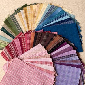 May include: A collection of square fabric swatches arranged in a fan shape, featuring a diverse array of colors including shades of blue, green, yellow, brown, red, pink, and purple, with various patterns such as plaids, checks, and solids.