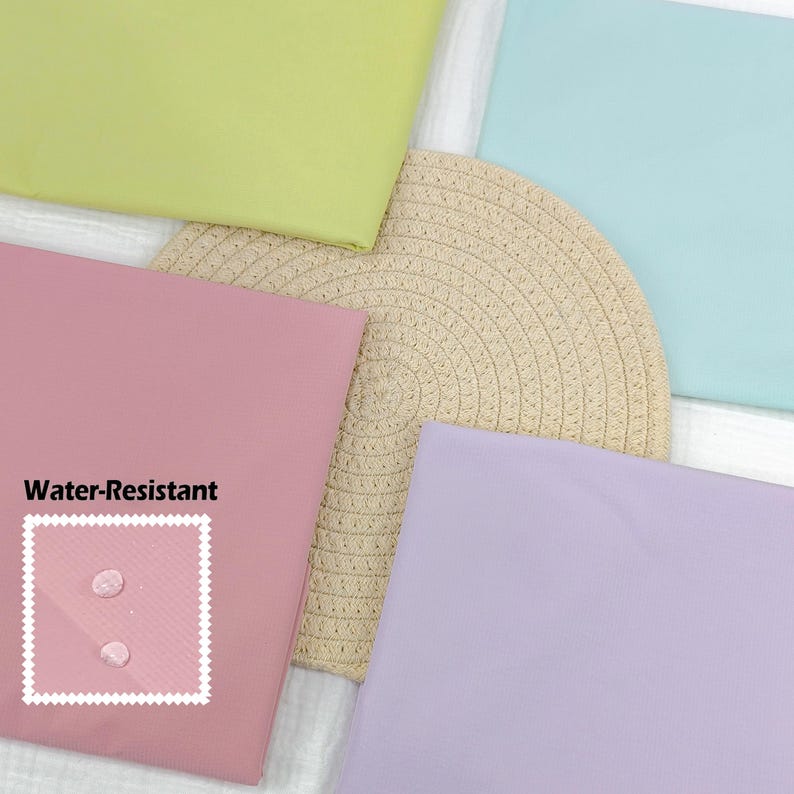 May include: A collection of pastel-colored placemats and a woven straw mat. The placemats are in shades of pink, green, blue, and purple. The pink placemat has a white box with the words "Water-Resistant" and a water droplet graphic.