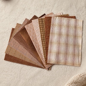 May include: A collection of rectangular fabric swatches arranged in a fan shape. The pieces feature various shades of brown, tan, and cream, with patterns including plaid, small dots, thin wavy lines, and solid textures in earthy tones.
