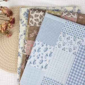 May include: A selection of patterned fabric pieces in various designs and colours. The fabrics include floral, gingham, and striped patterns in shades of blue, brown, pink, and cream. The fabrics are arranged in a layered composition.
