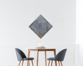 May include: A dining room with a white table and two gray chairs. A diamond-shaped painting with gold and gray abstract art hangs on the wall.