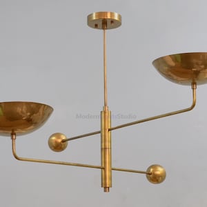 May include: A brass-coloured, mid-century modern chandelier with two bowl-shaped shades and spherical accents. The fixture is suspended from a ceiling mount and features a central column with horizontal arms.