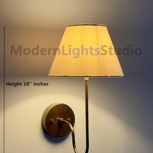 Puede incluir: Una lámpara de pared con una pantalla beige y un brazo metálico curvado. La lámpara mide 45,7 cm de alto y 25,4 cm de ancho. El texto "ModernLightsStudio" es visible en la imagen.
