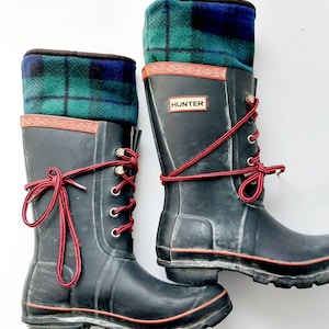 May include: Black Hunter wellington boots with red laces and tartan fleece boot toppers. The boots have a red trim and the Hunter logo. The tartan fleece is green, blue, and black.