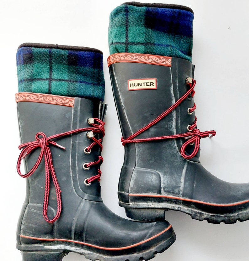 May include: Black Hunter wellington boots with red laces and tartan fleece boot toppers. The boots have a red trim and the Hunter logo. The tartan fleece is green, blue, and black.