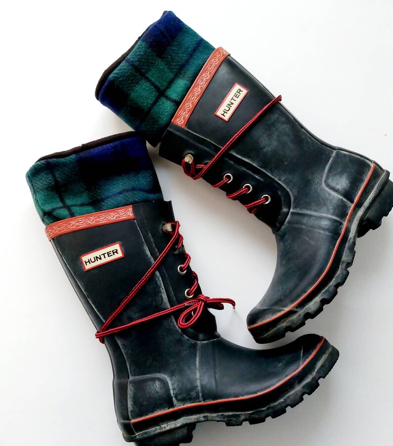 May include: Pair of black Hunter wellington boots with red laces and trim. The boots feature a green, blue, and black plaid fabric cuff. The word "HUNTER" is on a red rectangle on the side of each boot.