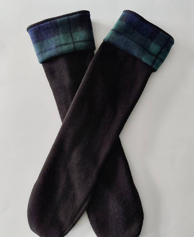 May include: A pair of black knee-high socks with a blue and green tartan cuff. The socks are made from a soft fabric and are designed to be worn over the calf. The tartan cuff adds a classic touch to the design.