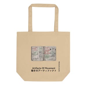 May include: A beige tote bag featuring a graphic of an open passport with various international travel stamps. Below the graphic, the text reads "Artifacts Of Movement" followed by Japanese characters and the vertical text "@ichinichi.studio".