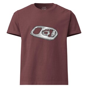 May include: A maroon short-sleeve t-shirt featuring a centered graphic illustration of a metallic silver soda can pull tab. The design shows the detailed texture and shape of the aluminum tab, including the ring and the torn metal edge.