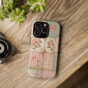 Peut inclure: Une coque de smartphone avec un motif patchwork composé de fleurs rose tendre et vert sauge, alternant avec des carreaux vichy rose clair et blanc. La coque présente une découpe noire pour l'appareil photo et recouvre tout le dos du téléphone.