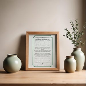 May include: A framed print featuring the text of Bilbo's Bath Song by J.R.R. Tolkien, displayed in a light wood frame with a green border. The poem is printed in black ink on a white background, centered within the frame, with clear, legible lettering.