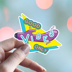 May include: A sticker with a purple and yellow design. The sticker features a purple object with the text "GOOD VIBES ONLY" in a yellow and blue font.