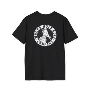 May include: A black short-sleeve t-shirt featuring a white circular graphic on the back. The design depicts a person in a pleated skirt and top holding a golf club, surrounded by the text WRONG HOLE GOLF COMPANY in a bold, circular font.