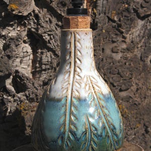 May include: A ceramic soap dispenser with a tapered neck and a wide base. The glaze transitions from a white top to a teal and green bottom, featuring carved leaf patterns throughout. It includes a cork stopper and a black plastic pump mechanism.
