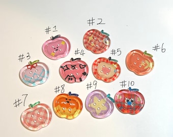 May include: A collection of ten apple-shaped buttons in various colors and patterns. Each button has a different design, including plaid, polka dots, and other decorative elements. The buttons are numbered from 1 to 10.