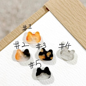 May include: Five cat-shaped buttons with two holes each, labeled #1 through #5. Button #1 is orange and white, #2 is orange, black, and white, #3 is black, orange, and white, #4 is translucent gray and white, and #5 is black and white.